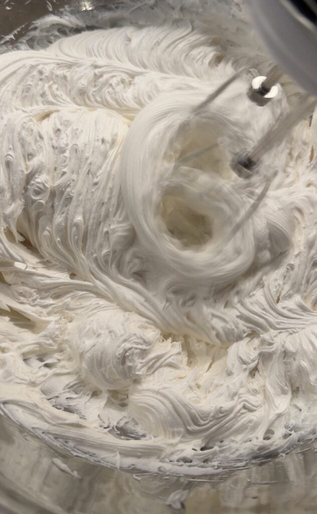 Store bought vanilla cream cheese frosting being whipped with a hand mixer until light and fluffy