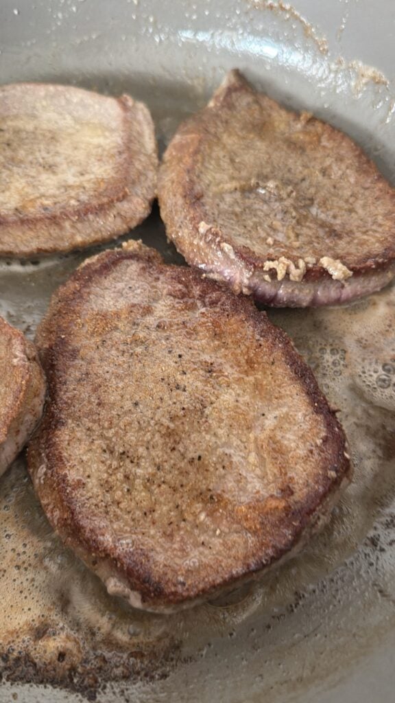 Round steaks browning in butter in a heavy skillet