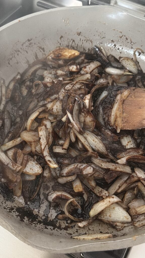 Sliced onions cooking in beef drippings for homemade round steak gravy