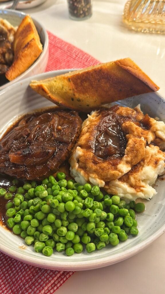 Tender round steak with onion gravy alongside peas and mashed potatoes