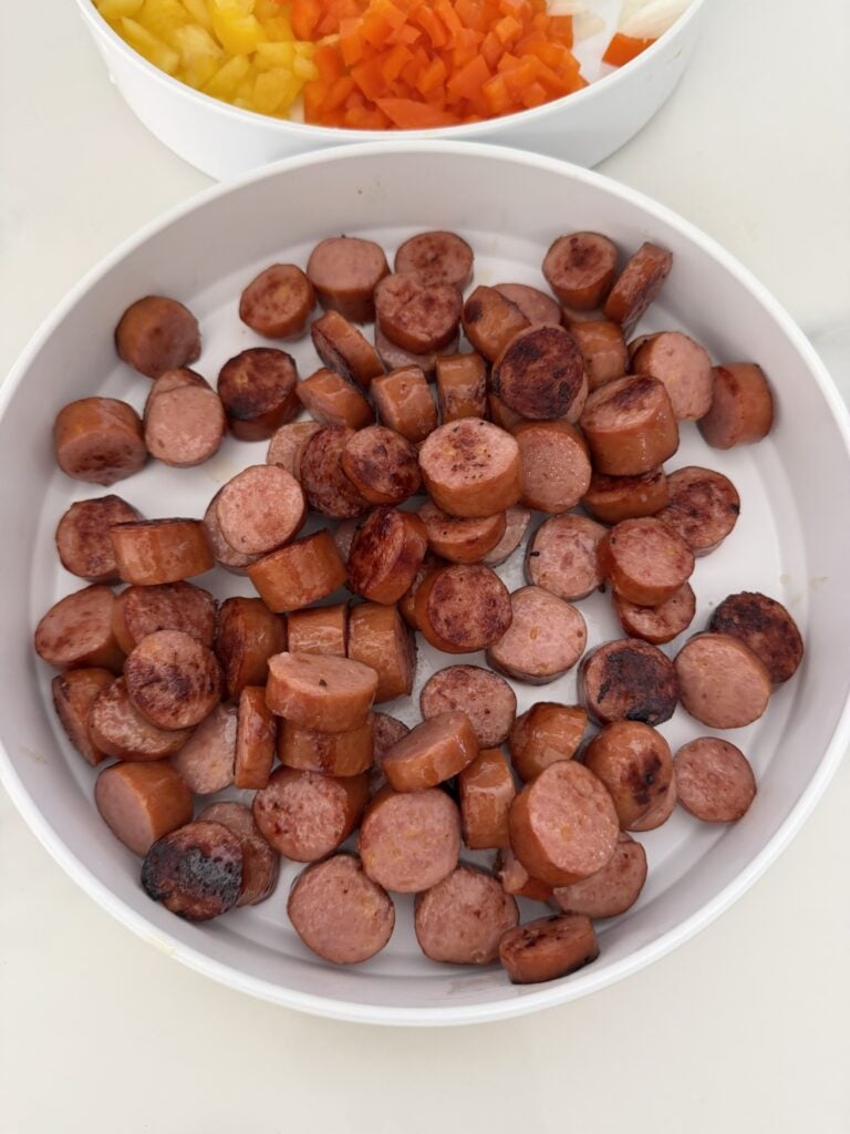 Sliced cheddar brats browned in a skillet before adding them to a baked rice casserole.