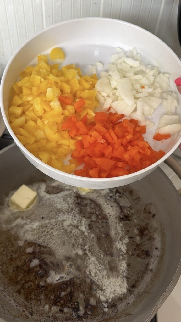 Diced peppers and onions over a pan of melting butter