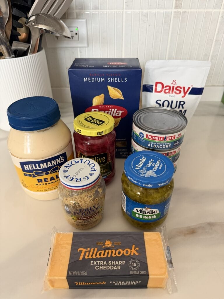 Ingredients for creamy tuna noodle pasta salad including tuna, shell pasta, cheddar, and dressing ingredients