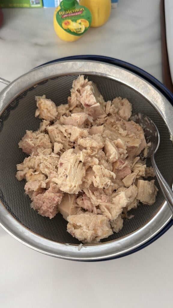 Canned tuna draining in a mesh strainer before making tuna noodle pasta salad