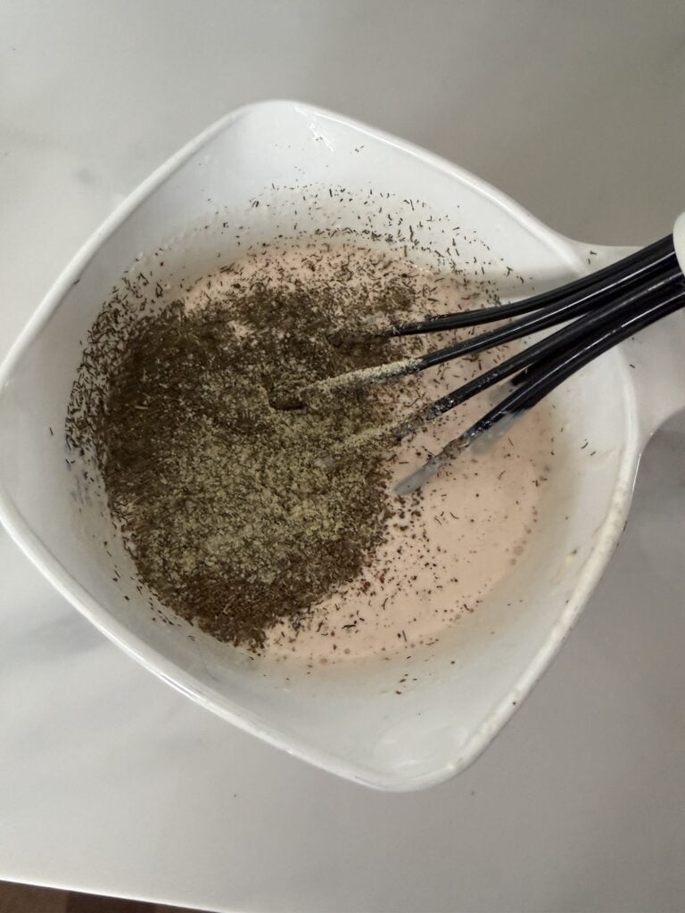 Mayonnaise, sour cream, Dijon mustard, and seasonings in a bowl with a whisk for tuna pasta salad dressing