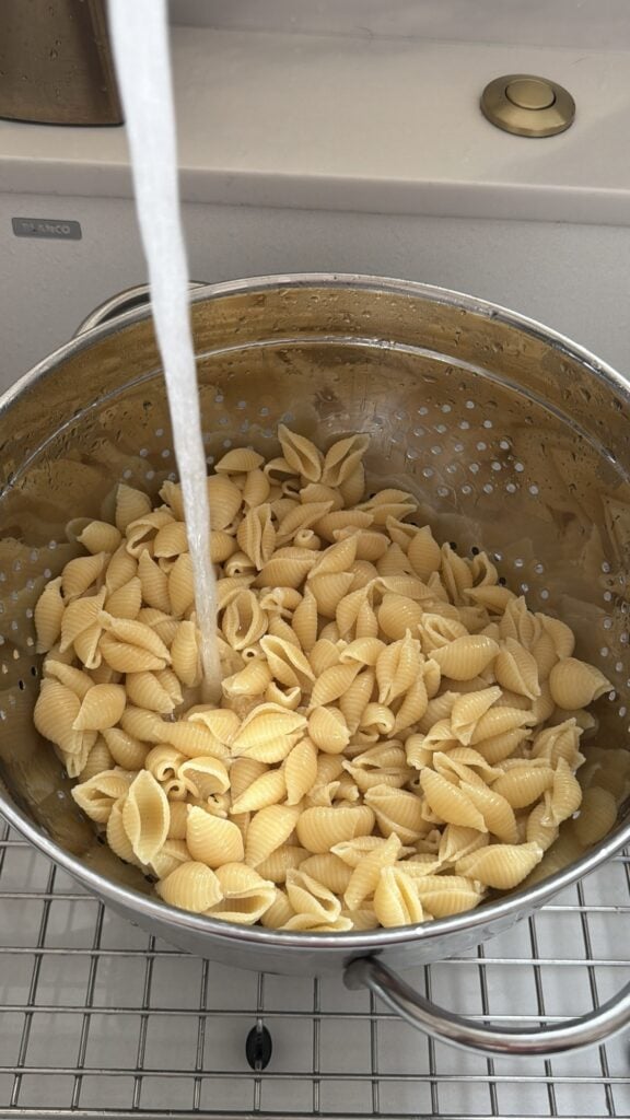 Water running over shell pasta cooked al dente for cold tuna pasta salad