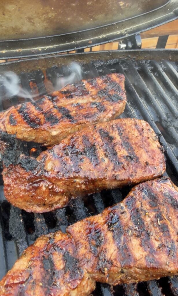 Sirloin steak developing a browned seared crust on a hot grill.