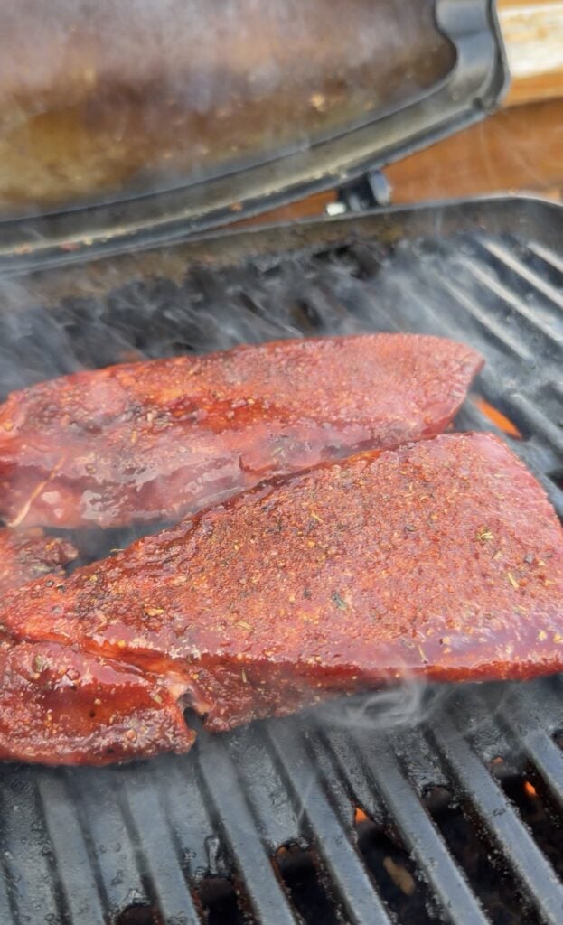 Seasoned sirloin steaks cooking on a hot outdoor grill.
