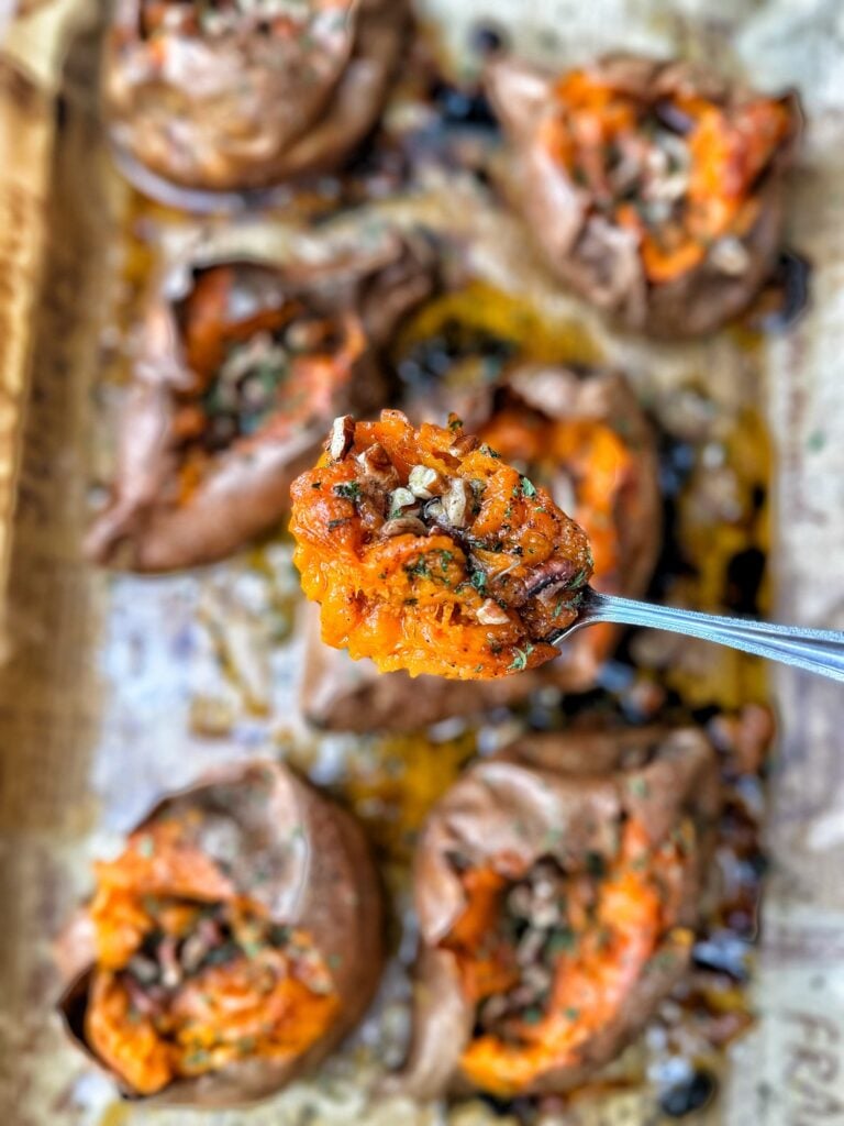 A spoon of baked sweet potato topped with savory maple butter, pecans, flaky salt, and chives