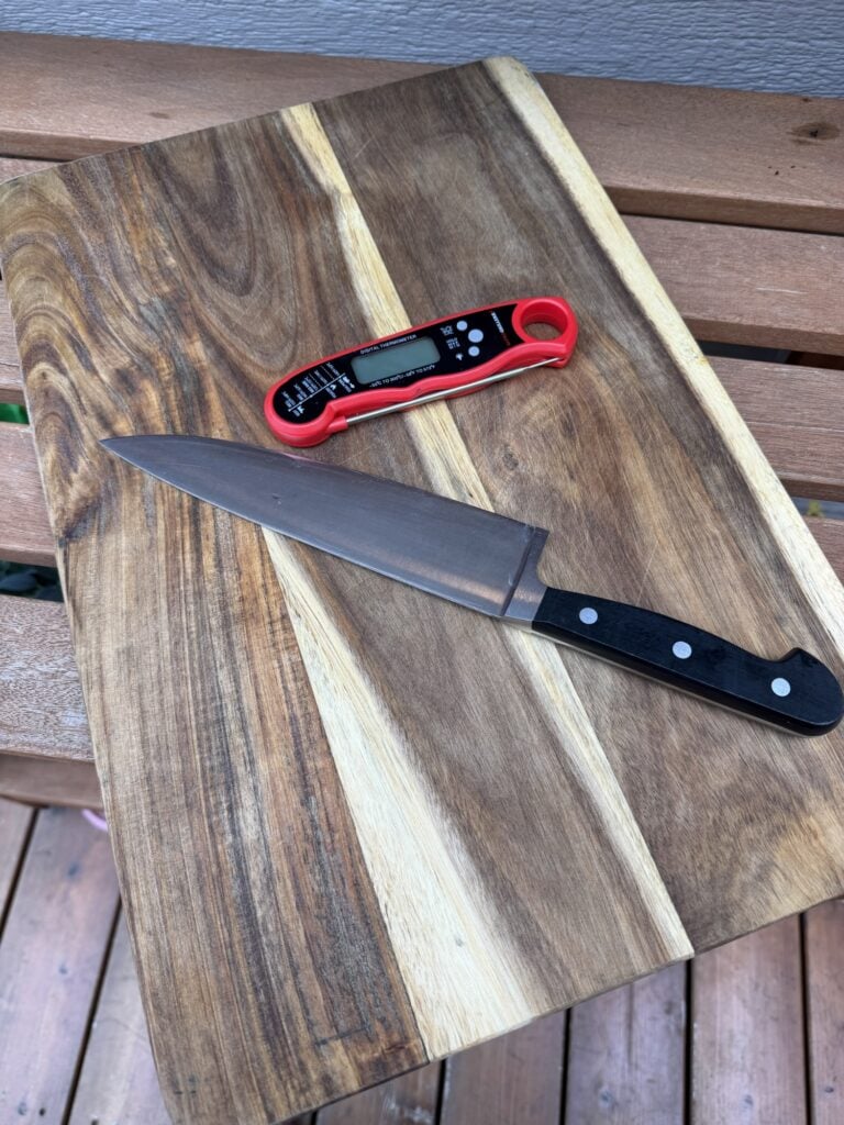 Meat thermometer, sharp carving knife, and large cutting board ready for preparing and carving a rib roast.