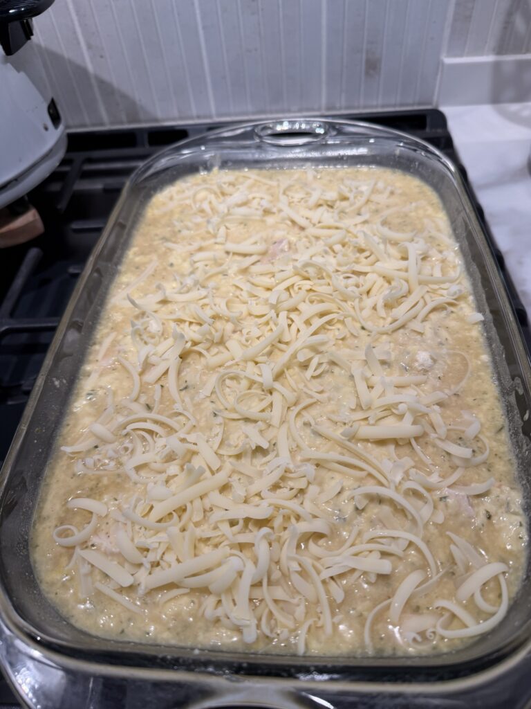 Creamy chicken and orzo mixture topped with cheese, ready for baking