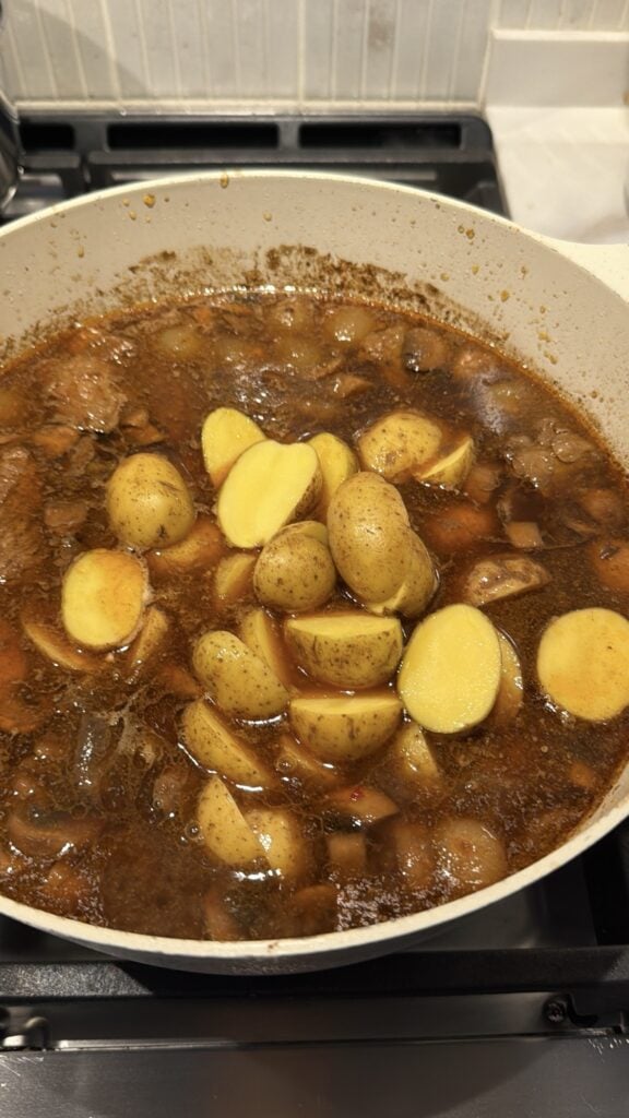 Unpeeled potato chunks added to a pot of simmering beef stew