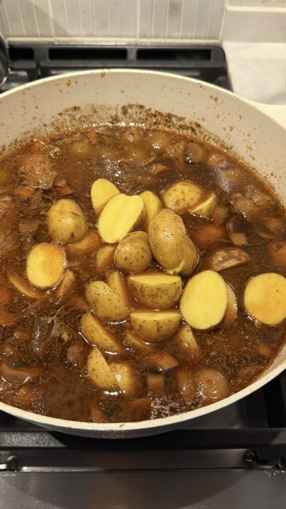 Pot of Halloween beef stew gently simmering on the stove with potatoes and mushrooms visible