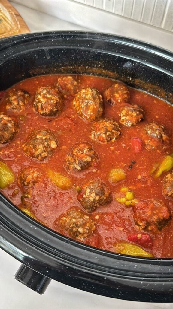 a slow cooker of meatballs with yellow peppers and red sauce