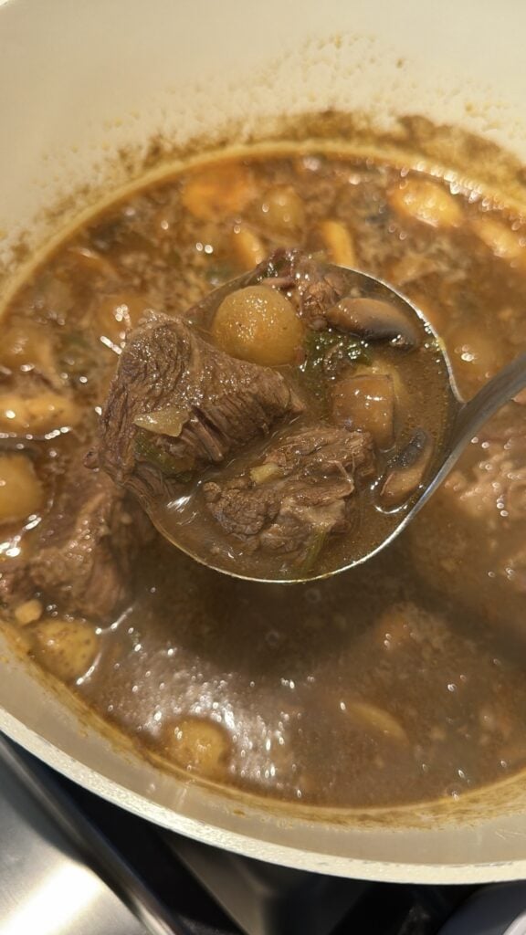 Spicy beef and potato stew being ladled into a bowl over a spoonful of white rice