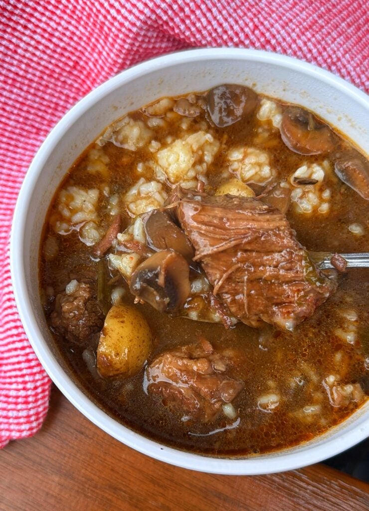 Bowl of spicy beef stew with potatoes, mushrooms, cocktail onions, and a spoonful of white rice