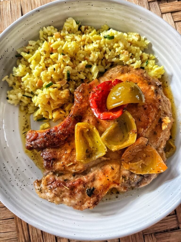 pork chops with a bone on a plate with yellow rice and cherry peppers