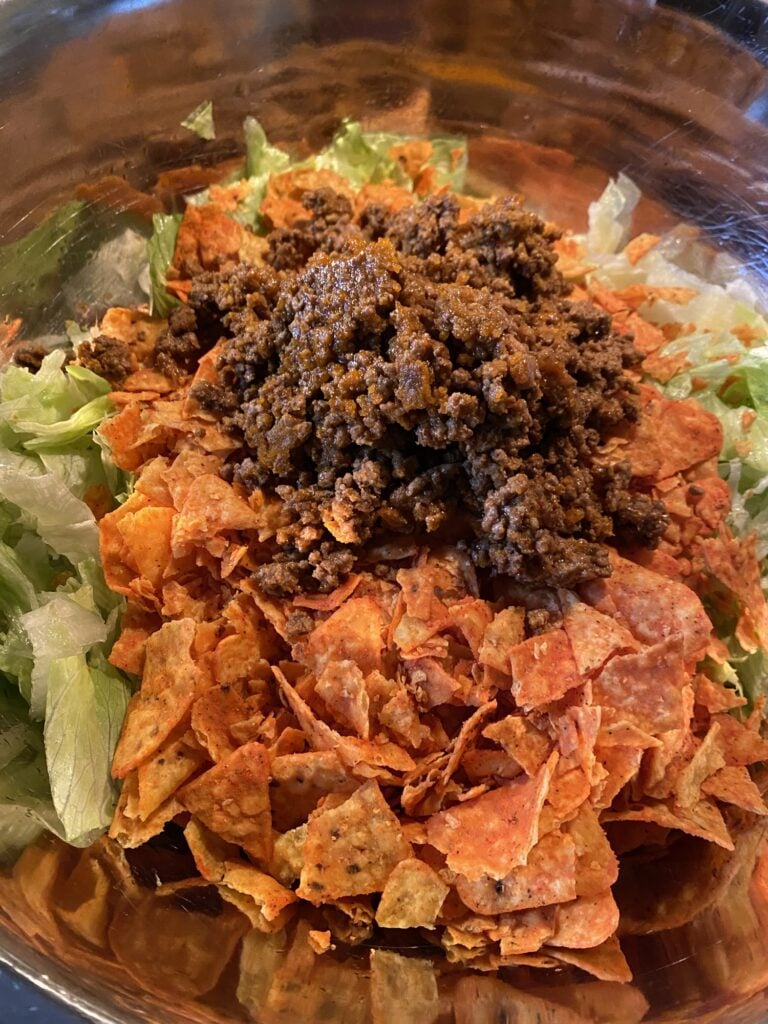 Seasoned ground beef and crushed Doritos added to iceberg lettuce for Midwestern Taco Salad