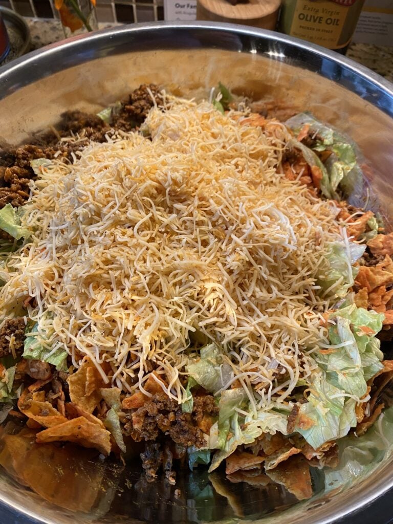 Shredded cheese added to Midwestern Taco Salad with ground beef, Doritos, and iceberg lettuce