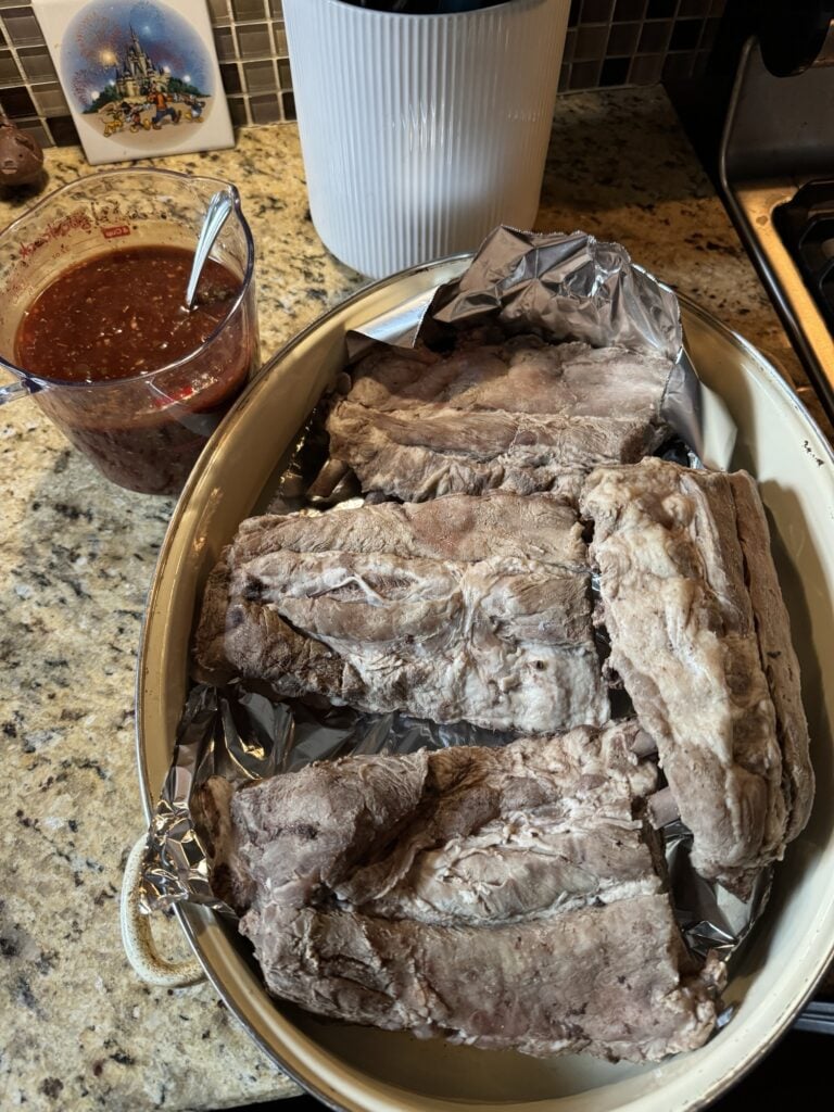 Pork ribs next to a cup of barbecue sauce