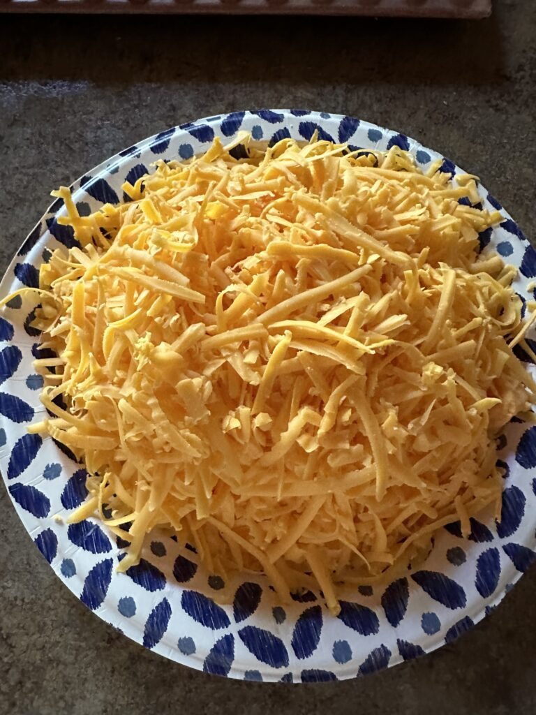 a paper plate with a mound of shredded sharp cheddar cheese
