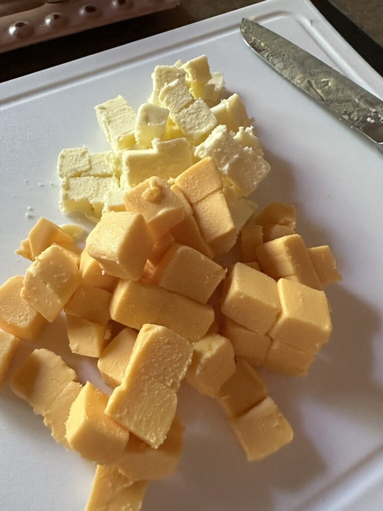 cubed velveeta cheese and cubed butter on a cutting board