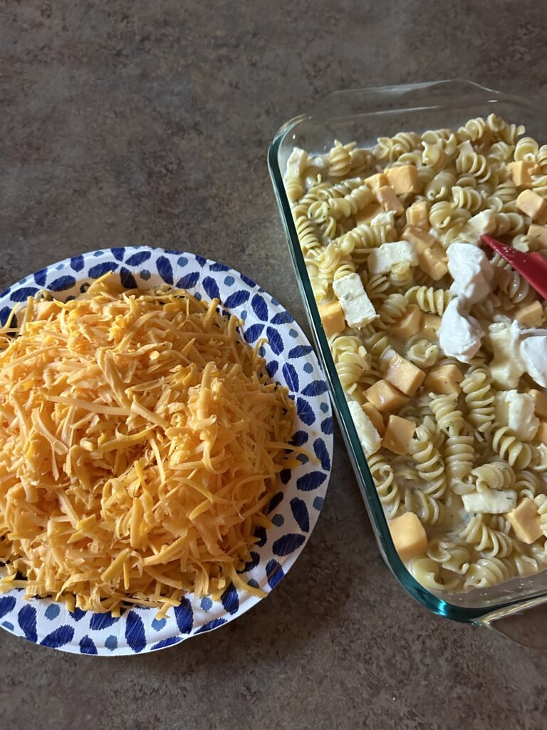 a plate of sharp cheddar cheese next to the patially assembled macaroni and cheese casserole