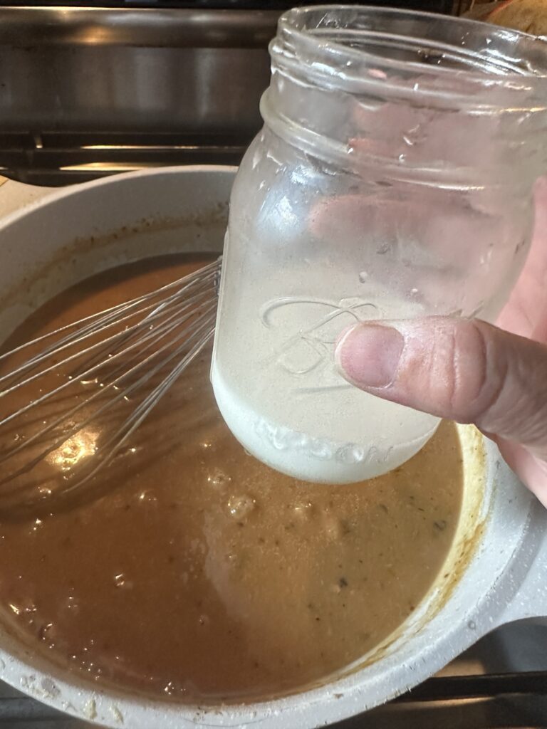 a jar of slurry, that is white, above the pan of gravy.