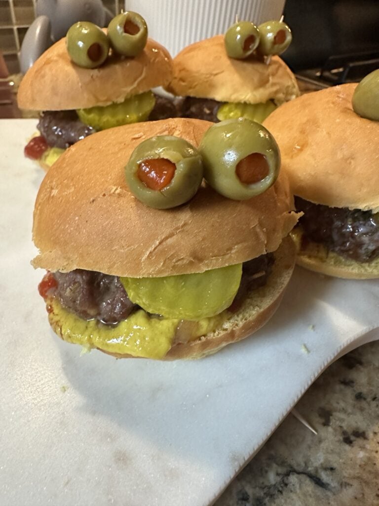 Cute Halloween monster burger decorated with olive eyes and pickle tongue