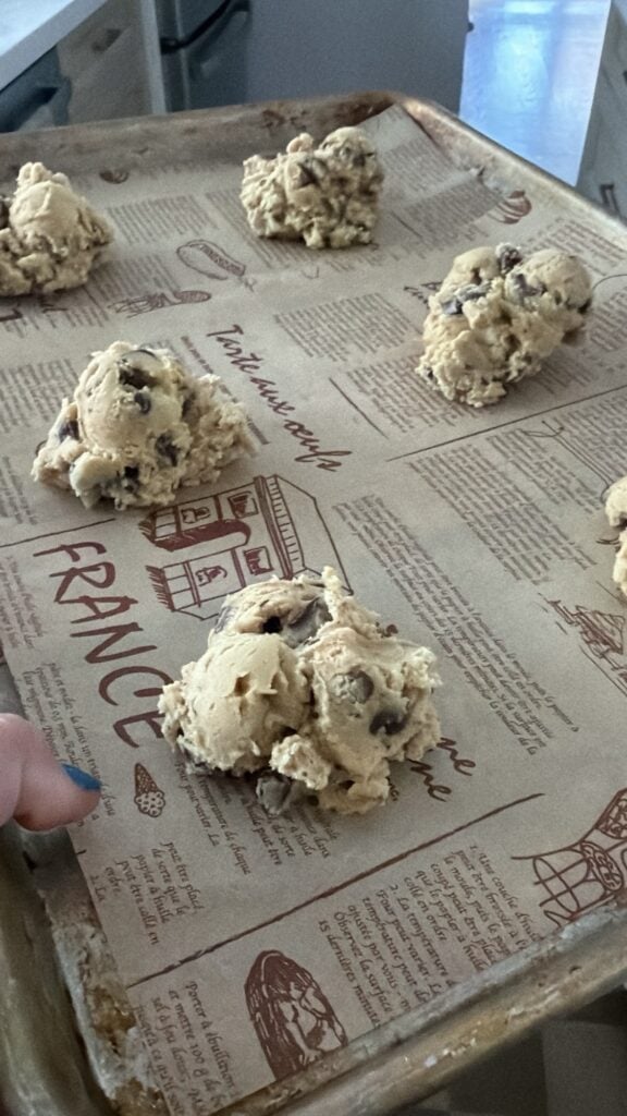 Jumbo portions of chilled chocolate chip cookie dough arranged on a parchment-lined baking sheet.