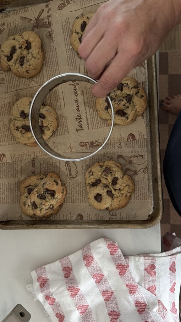 Round cookie cutter used to shape a hot jumbo chocolate chip cookie into a perfect circle.