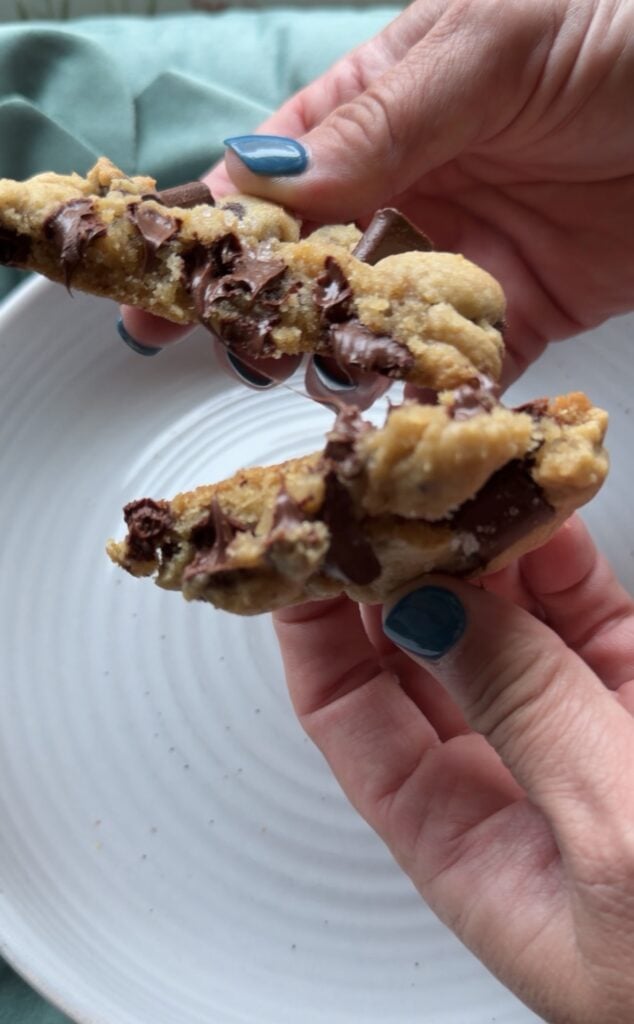 Thick jumbo chocolate chip cookie broken open to show a soft and chewy center with melted chocolate.