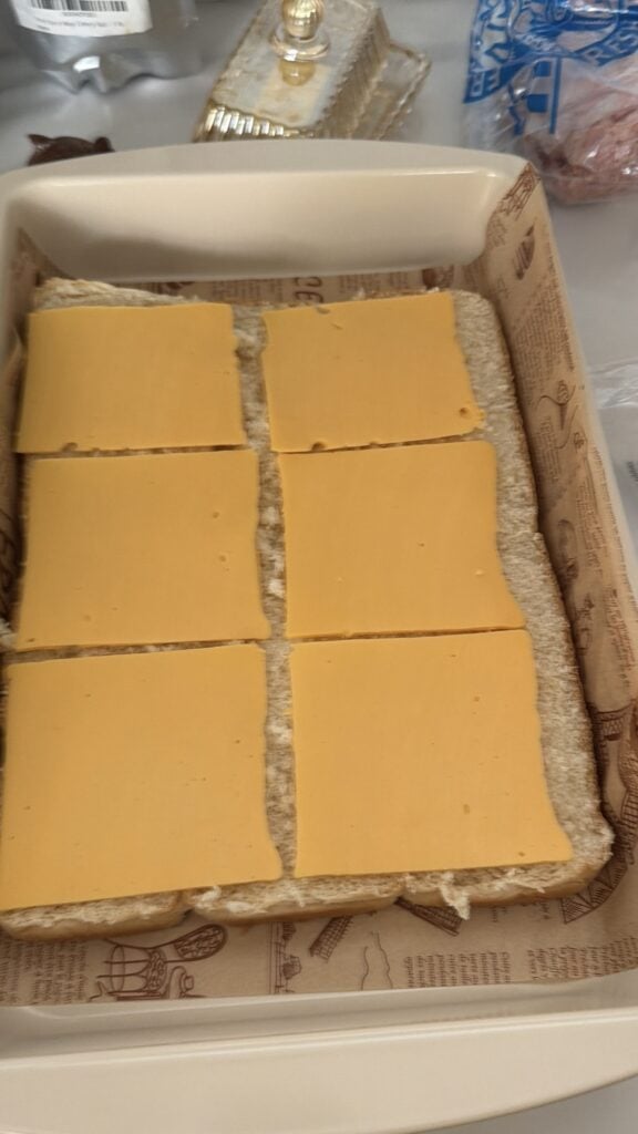 Slices of cheese on a sheet of slider bun bottoms