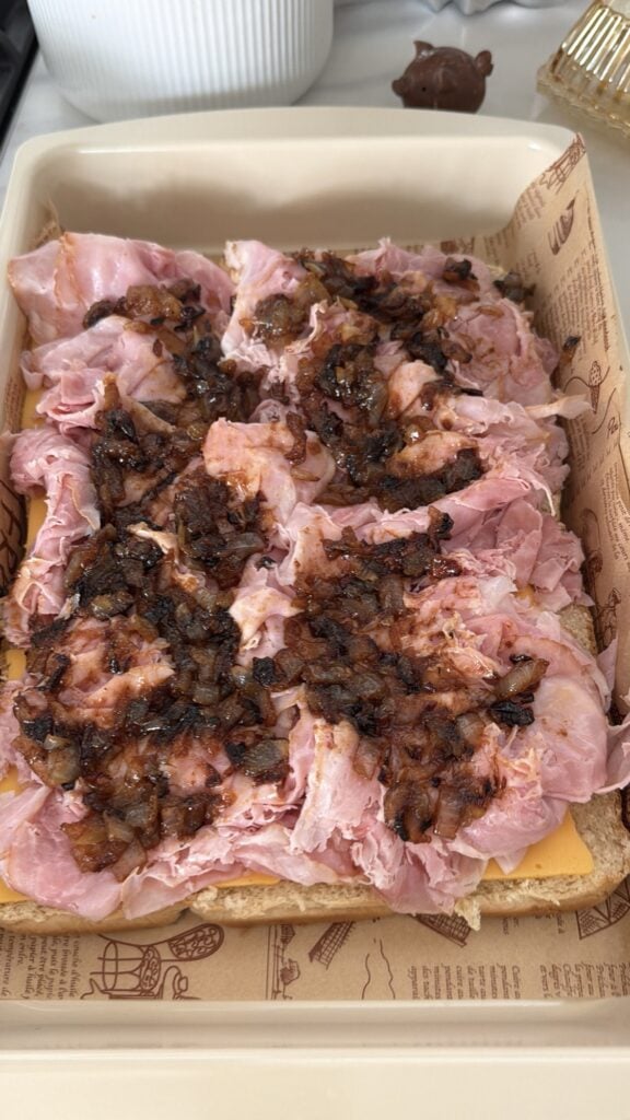 Caramelized onions on ham and cheese sliders before baking