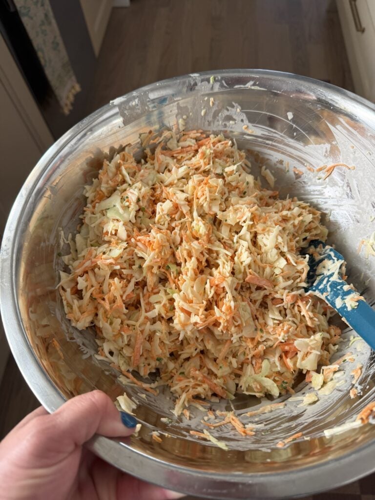 Finely chopped cabbage, carrots and onion being tossed with creamy coleslaw dressing