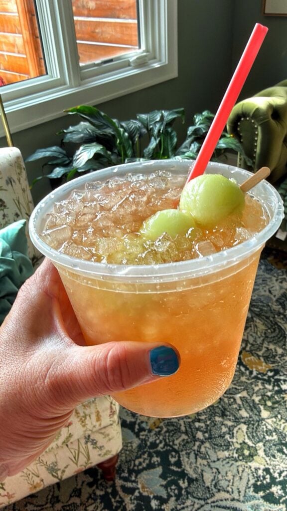 Honey Deuce cocktail made with vodka, lemonade, raspberry liqueur, and frozen honeydew melon balls in a deli container