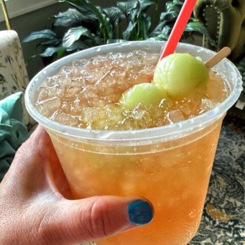 Honey Deuce cocktail made with vodka, lemonade, raspberry liqueur and frozen honeydew melon balls in a deli container