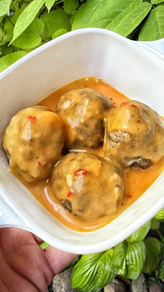 four meatballs in a dish, covered in a cheddar cheese sauce