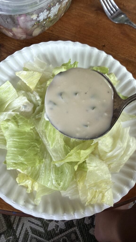 Creamy homemade dressing being spooned over crisp iceberg lettuce