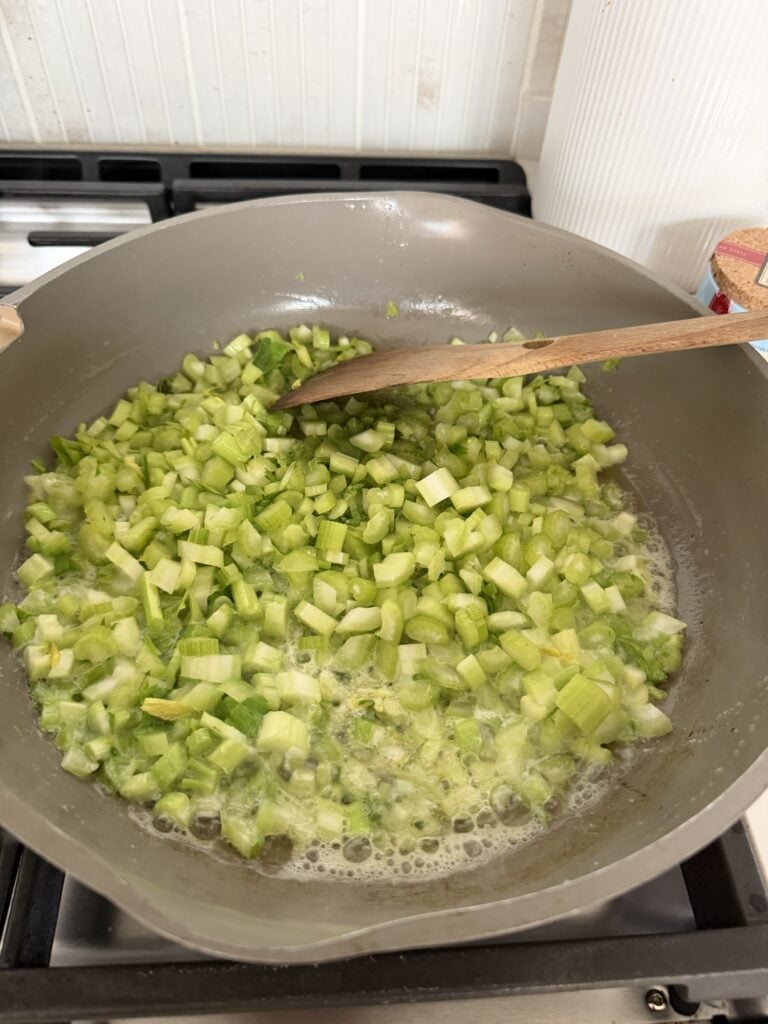 Fresh sliced celery and onions sautéing in butter in a skillet for homemade celery soup.