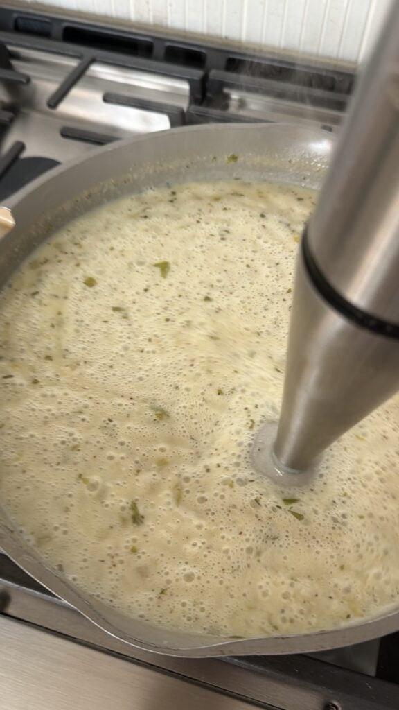 Cream of celery soup being partially blended with an immersion blender directly in the skillet.