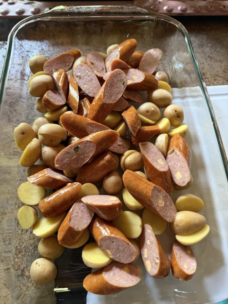 Baby potatoes, sliced smoked sausage, and sweet onions seasoned in a casserole dish before roasting.