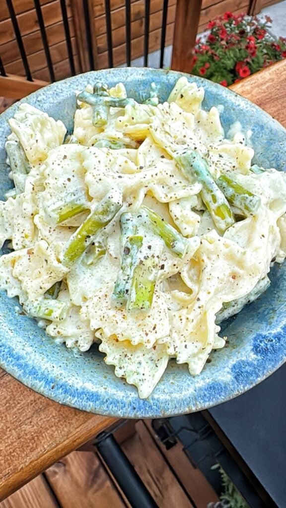 bow tie noodles with asparagus, black pepper and a creamy sauce in a blue bowl