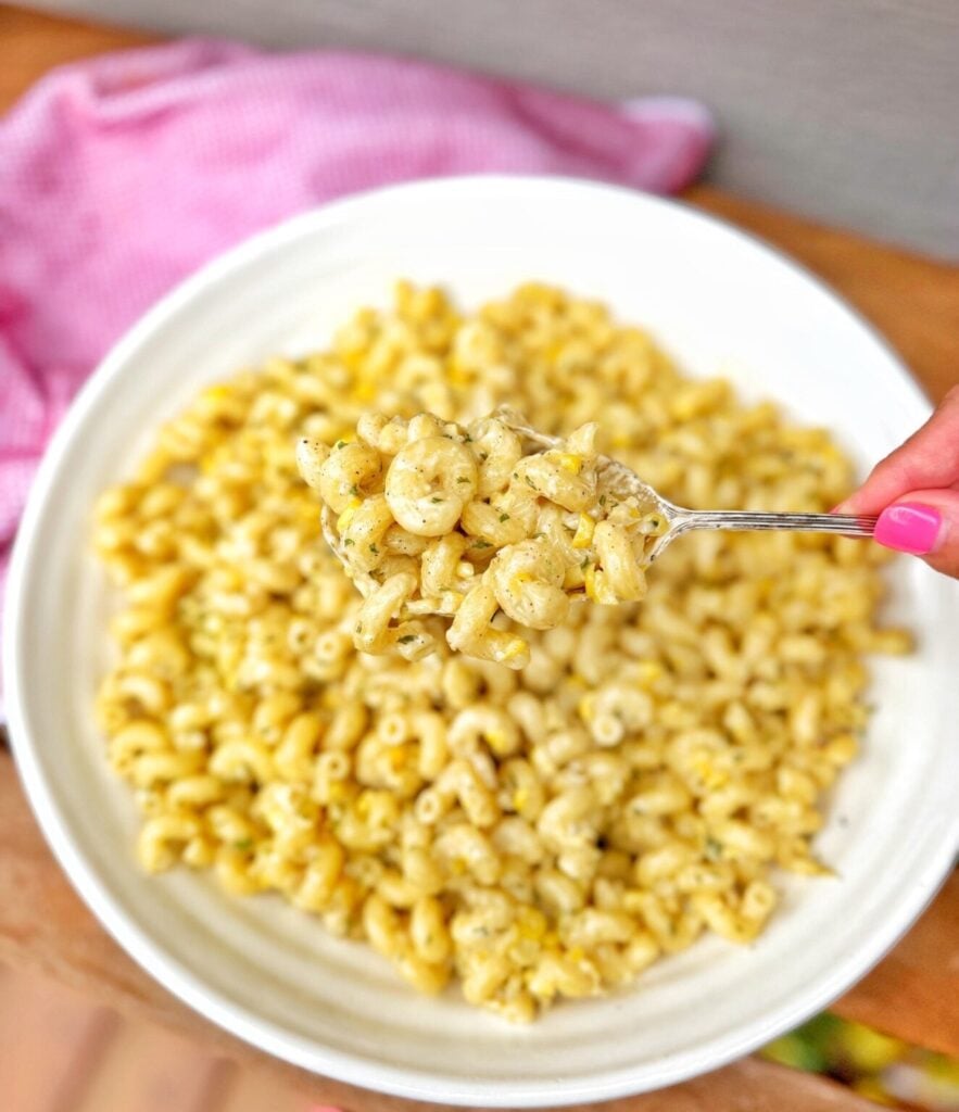 corn and pasta in a white bowl with a large spoon of the pasta showing with the creamy sauce