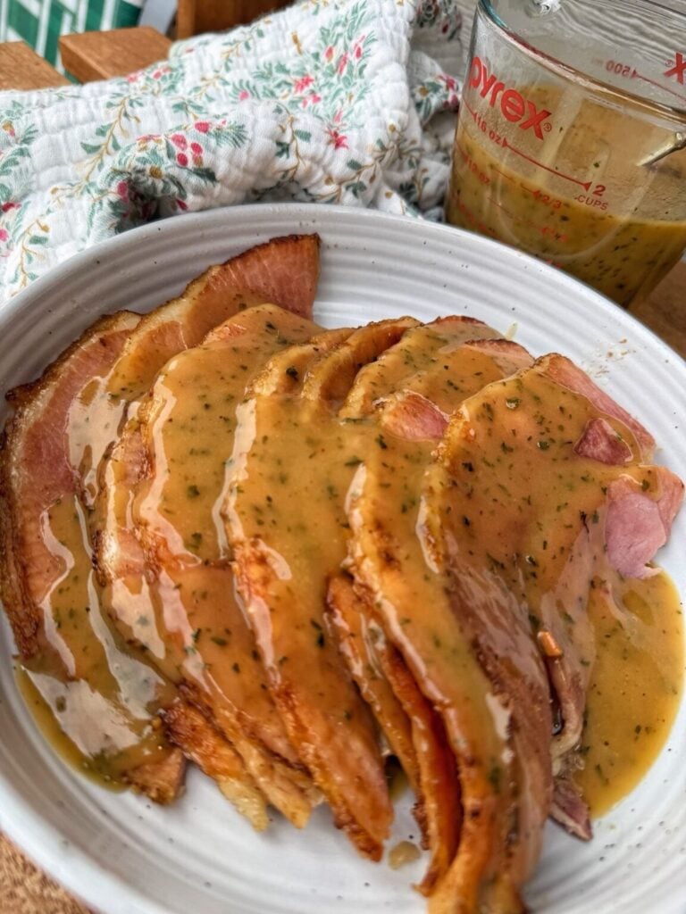 ham slices with a savory mustard based gravy spooned over the slices arranged on a plate
