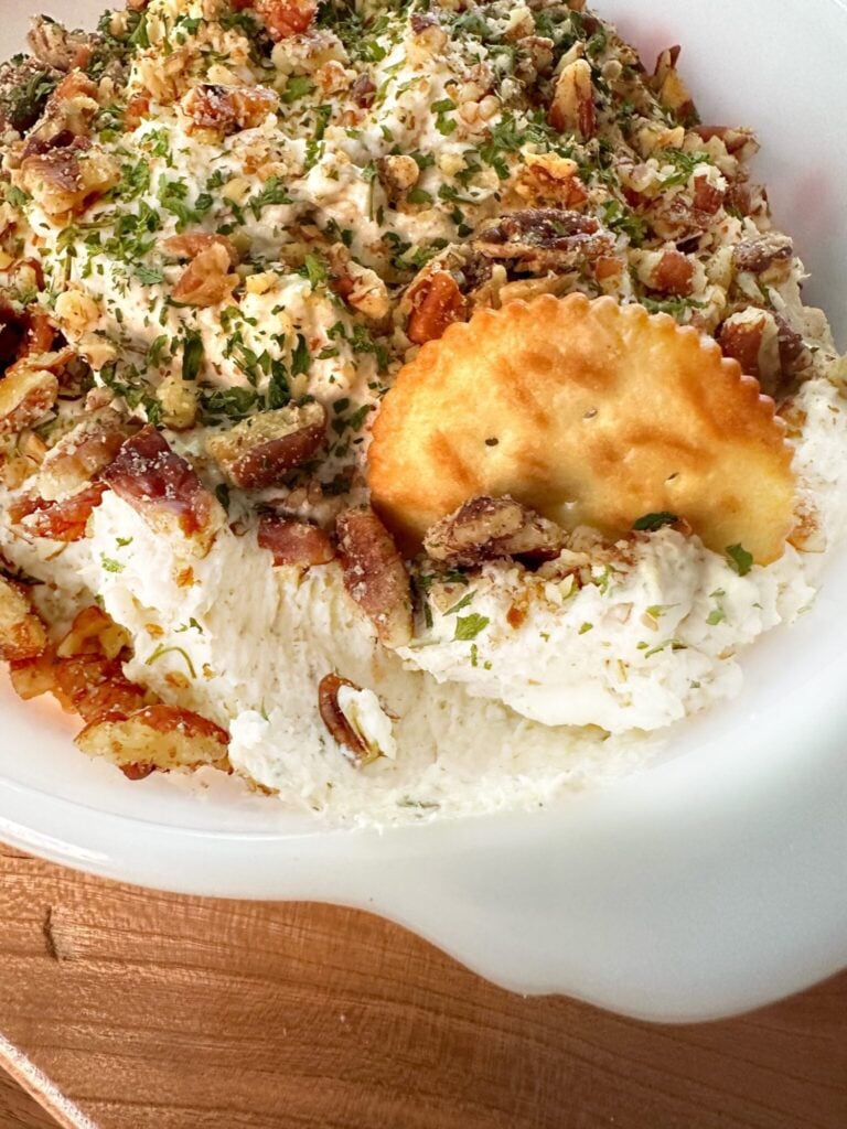 Creamy chicken spread topped with chopped pecans and parsley with a buttery cracker