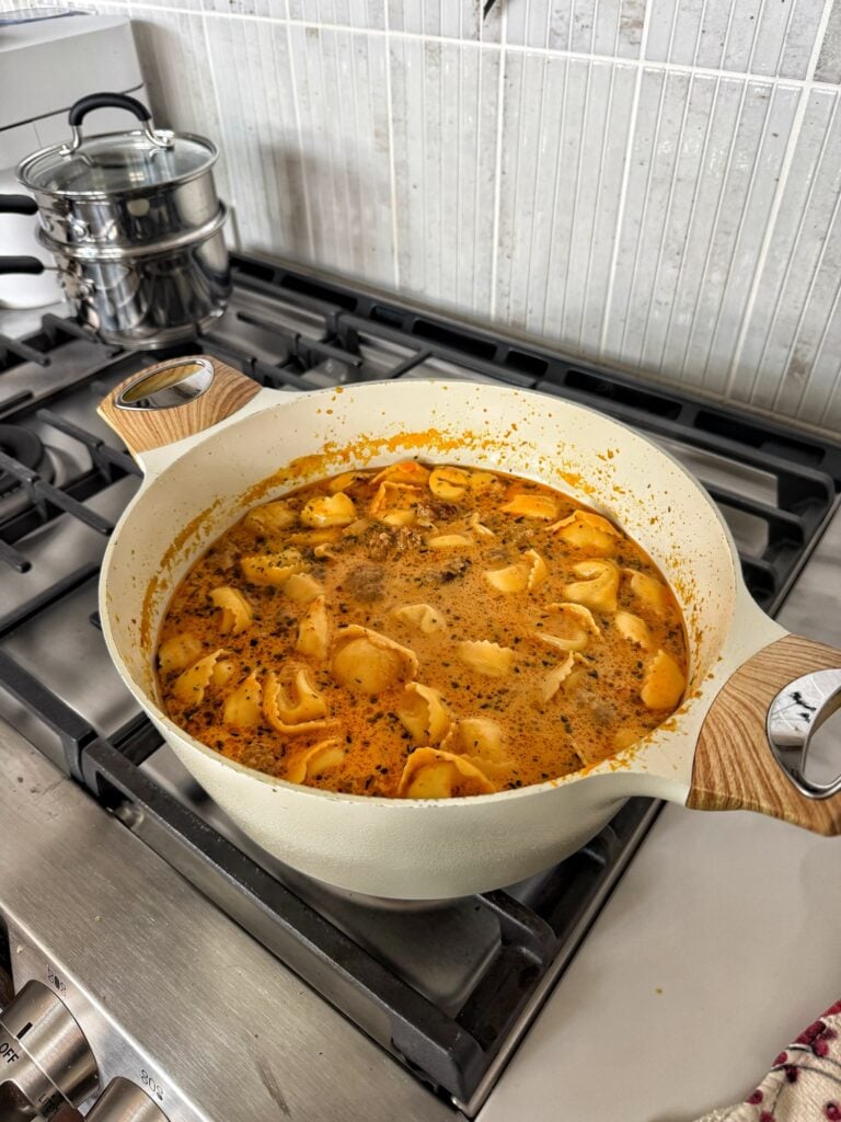 Pumpkin sausage tortellini soup simmering in a Dutch oven for a cozy Halloween dinner.