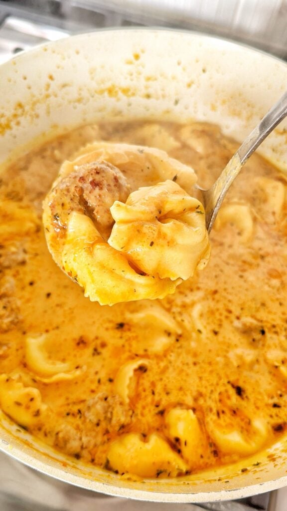 pumpkin and sausage soup with tortellini in a ladle over the pot.
