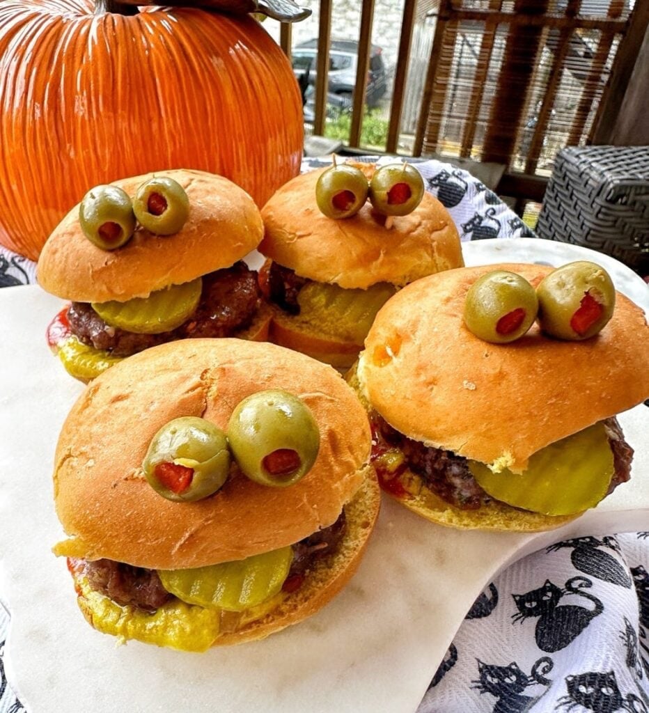 slider burgers made to look festive for halloween with olive eyeballs and pickle tongues