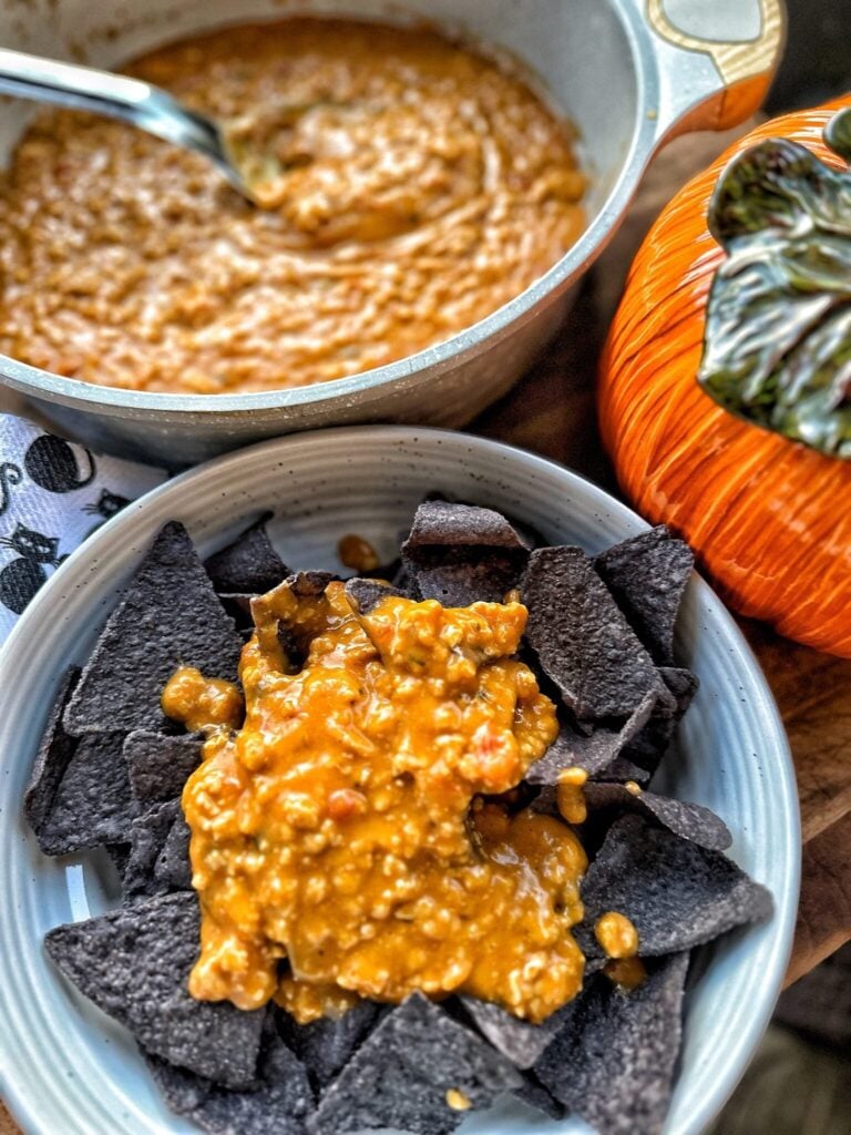 a pan of queso with ground chicken and a plate of dark blue tortilla chips topped with the orange queso to look festive for halloween
